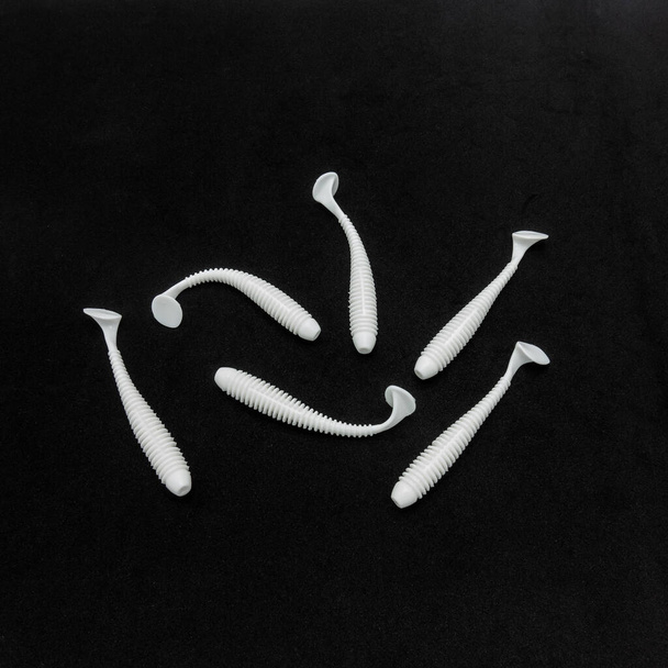 Accessori da pesca. Esche in silicone bianco che sembrano piccoli vermi. Bordi a costine, forma flessibile. Fondo nero. Vista dall'alto. Primo piano - Foto, immagini