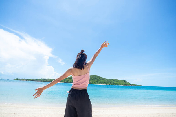 ピンクのタンクトップを身に着けている女性の日焼け肌と空に突き出た腕を持つわらの帽子。海と新鮮な空を見ています。夏の旅行。リラックス、休日と熱帯、快適なコンセプト. - 写真・画像