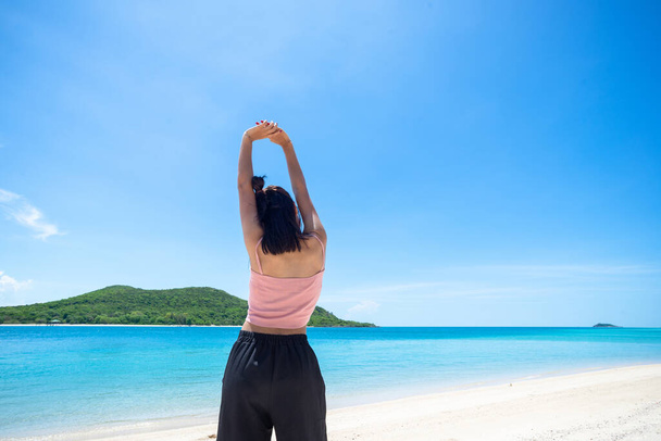 ピンクのタンクトップを身に着けている女性の日焼け肌と空に突き出た腕を持つわらの帽子。海と新鮮な空を見ています。夏の旅行。リラックス、休日と熱帯、快適なコンセプト. - 写真・画像