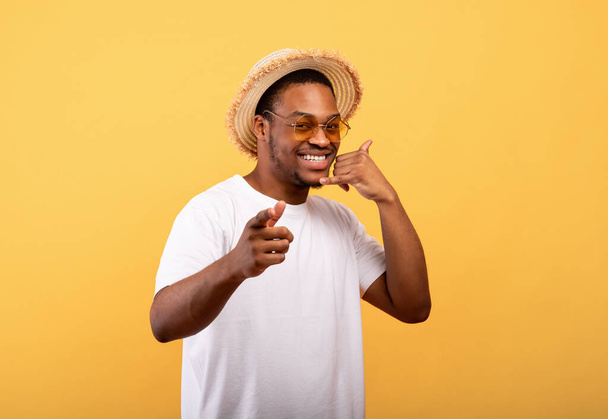 chico afroamericano en traje de verano de moda que muestra el gesto de LLAME ME, sonriendo a la cámara en el fondo amarillo - Foto, imagen