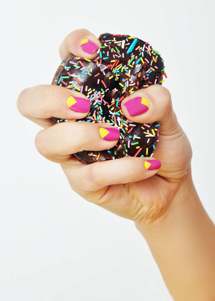 A vertical closeup shot of female hands with patterned nail polish holding a donut - Foto, afbeelding