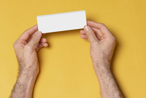 A male's hands holding a small white paper box isolated on a yellow background - Фото, зображення