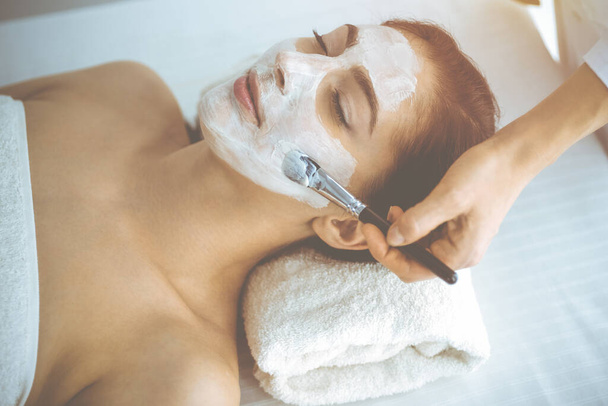 Beautiful brunette woman enjoying applying cosmetic mask with closed eyes. Relaxing treatment in medicine and spa concepts - Φωτογραφία, εικόνα
