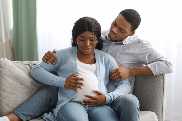 Pregnant woman having labor pains, sitting by husband on couch - Zdjęcie, obraz