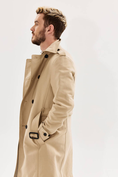 man holding hands in pockets of beige coat side view light background - Foto, imagen
