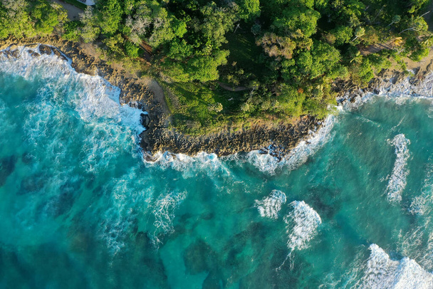 Vzdušný záběr útesů pokrytých zelení obklopených mořem pod slunečním světlem - Fotografie, Obrázek