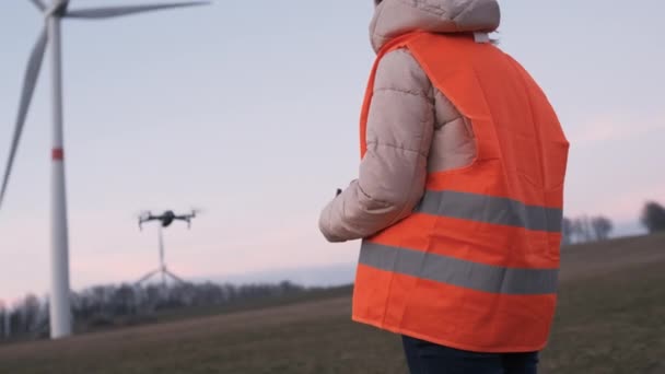 Engenheira usa um drone para verificar o desempenho do sistema de turbina selvagem ou moinho de vento ao pôr do sol. - Filmagem, Vídeo