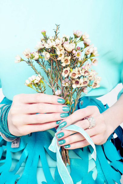 A vertical closeup shot of female hands with blue nail polish holding a bouquet - Fotó, kép