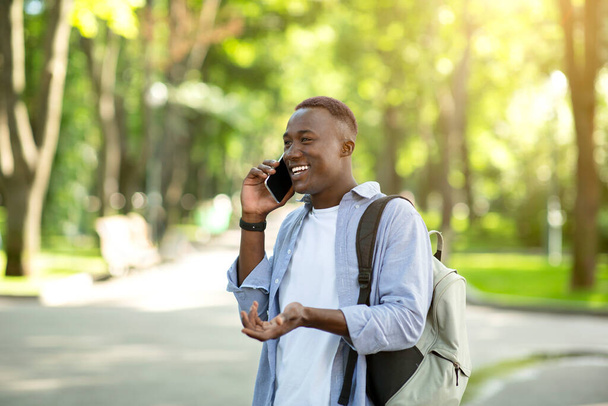 Šťastný černoch s batohem mluví na mobilním telefonu v městském parku, volné místo - Fotografie, Obrázek