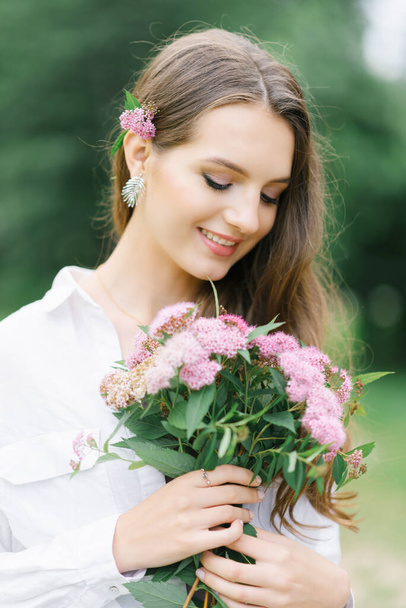 Nahaufnahme einer schönen jungen Frau mit rosa Blüten an einem sonnigen Tag im Park. Eine glückliche Frau bekam von ihrem Freund einen Strauß Gartenblumen geschenkt - Foto, Bild