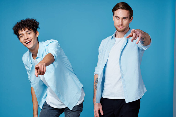 guys in identical shirts and a t-shirt on a blue background friends gesticulate with their hands - Фото, изображение