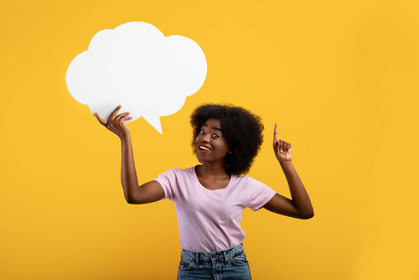 Inspired african american lady having idea, holding blank speech bubble and pointing finger up, yellow background - Photo, Image