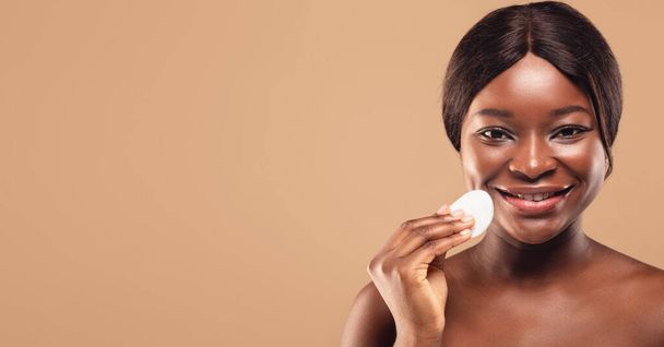 Concepto de cuidado de la piel. Hermosa mujer afroamericana limpiando la cara con almohadilla de algodón - Foto, imagen
