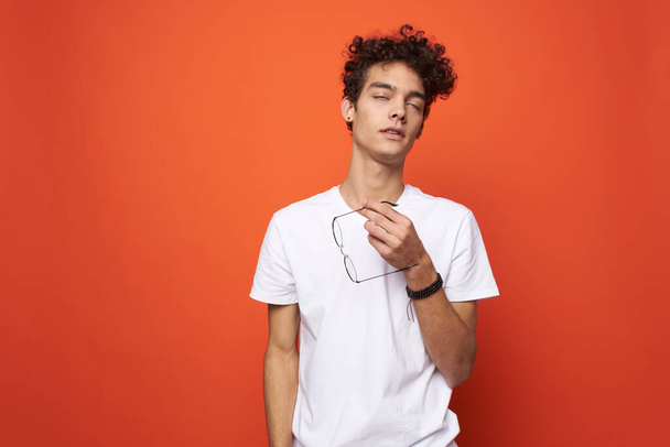 man with curly hair and glasses white t-shirt licks orange background - Foto, Imagen