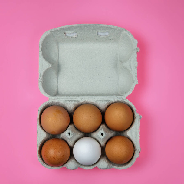 Huevos marrones con un huevo blanco en una bandeja de papel sobre una superficie rosa - Foto, imagen