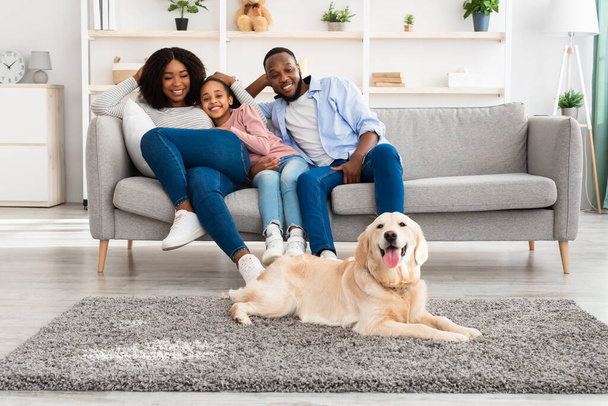 Χαρούμενη μαύρη οικογένεια που κάθεται στο σαλόνι με το σκυλί - Φωτογραφία, εικόνα