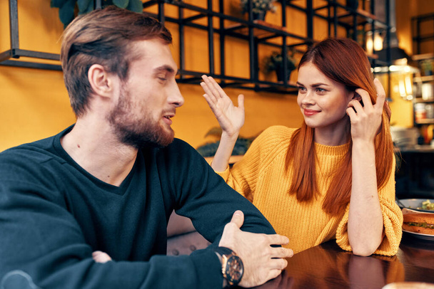 hombre y mujer están sentados en un café a la mesa y haciendo gestos con sus manos amigos emociones diversión interior - Foto, Imagen