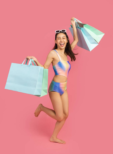 Beautiful, Sexy asian woman in  bikini and smiling standing on pink background isolated .Summer vocation happy trip.She smiling and  happy shopping bags. - Foto, Bild