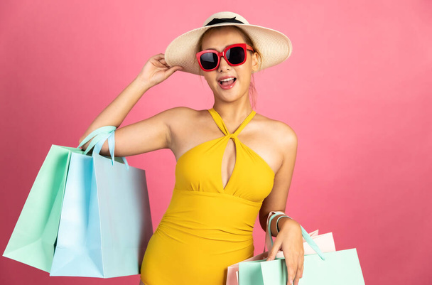 Beautiful, Sexy asian woman in  bikini and smiling standing on pink background isolated .Summer vocation happy trip.She smiling and  happy shopping bags. - Fotografie, Obrázek