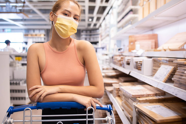 young asian woman with medical mask looking and shopping in the warehouse store during coronavirus (covid-19) pandemic. .After quarantine due to coronavirus outbreak with new normal lifestyle. - 写真・画像