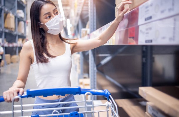 young asian woman with medical mask looking and shopping in the warehouse store during coronavirus (covid-19) pandemic. .After quarantine due to coronavirus outbreak with new normal lifestyle. - Photo, image