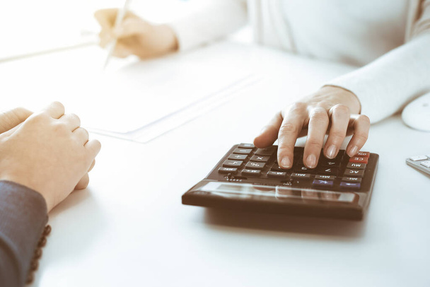 Accountant checking financial statement or counting by calculator income for tax form, hands closeup. Business woman sitting and working with colleague at the desk in office. Tax and Audit concept - Фото, изображение
