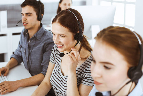 Casual dressed young woman using headset and computer while talking with customers online. Group of operators at work. Call center, business concept - Φωτογραφία, εικόνα