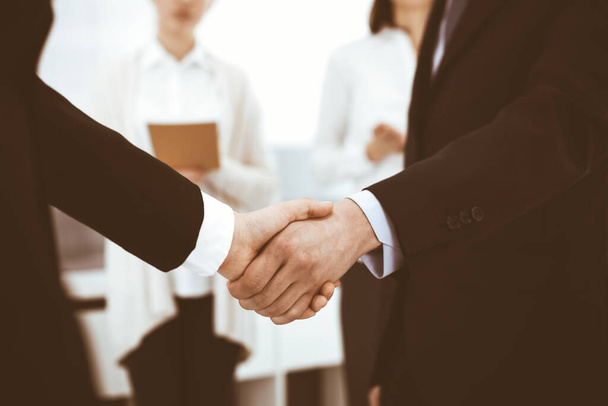 Businessman and woman shaking hands with colleagues at the background. Handshake at meeting in office. Concept of success in business - Foto, afbeelding