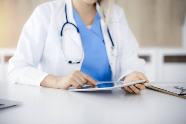 Unknown woman-doctor sitting in sunny clinic and using tablet pc, close-up. Data and best service in medicine - Foto, Imagem