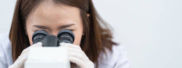 Una giovane scienziata con un camice da laboratorio che guarda attraverso un microscopio in un laboratorio per fare ricerca e sperimentazione. Scienziato che lavora in un laboratorio. Foto stock di istruzione - Foto, immagini