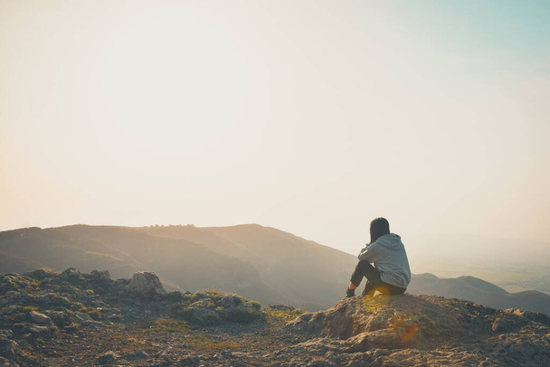 Жінка сидить на самоті і дивиться навколо краю скелі з сонячним фоном неба. Поняття самотності, пригод і способу життя
. - Фото, зображення