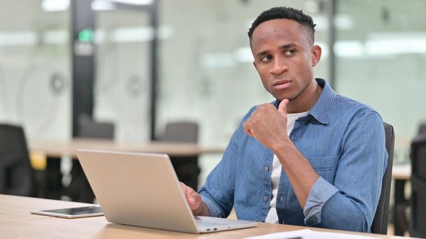 Hombre africano casual Pensando y trabajando en el ordenador portátil en la oficina  - Foto, Imagen