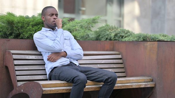Doente jovem africano tosse no banco ao ar livre - Foto, Imagem