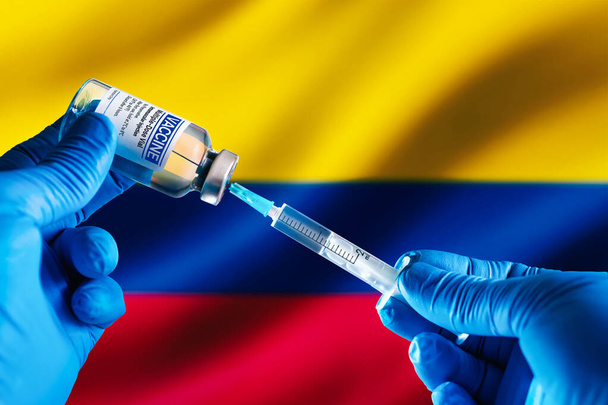 Médico preparando vial de vacuna inyectable para el plan de vacunación contra enfermedades en Colombia. Dosis inyectable de vacuna en jeringa para prevención de infecciones frente a la bandera de Colombia - Foto, Imagen