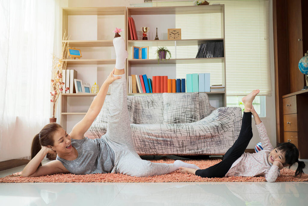 Beautiful young woman and her charming little daughter are smiling while doing yoga together at home - Photo, image