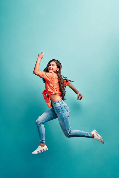 Beautiful young attractive careless girl jumping having fun fooling flying isolated on bright vivid turquoise color background. Concept of carefree and cheerful mood.Full length body size view. - Фото, изображение