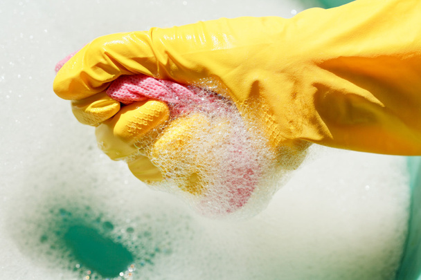 Hand in gelbem Gummihandschuh ringt nassen Staubwedel aus - Foto, Bild