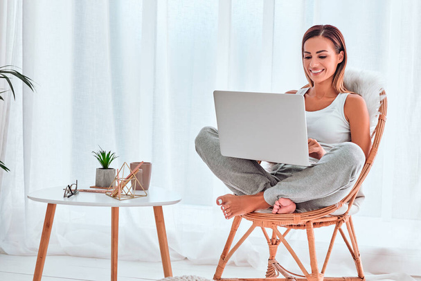 Pretty lady working on her laptop while sitting in an armchair. Copy space - Foto, Imagen