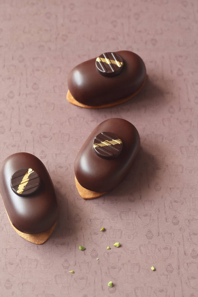 Hedendaagse Mini Mousse Cakes, bedekt met chocolade, versierd met chocolade elementen, op een bruine achtergrond. - Foto, afbeelding