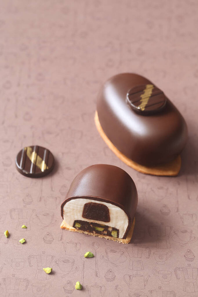 Hedendaagse Mini Mousse Cakes, bedekt met chocolade, versierd met chocolade elementen, op een bruine achtergrond. - Foto, afbeelding