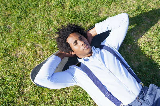 黒人実業家はスケートボードで芝生の上で休んでいる - 写真・画像