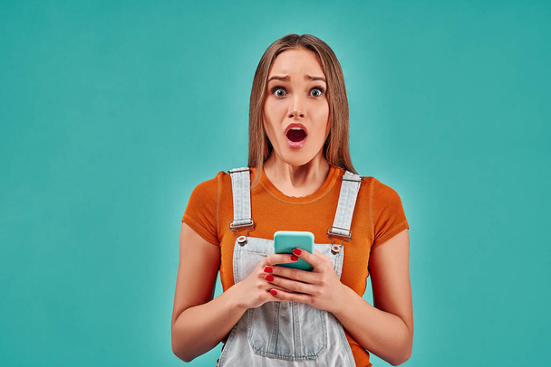 Shocked woman looking at mobile phone isolated on blue background. Copy space - Fotó, kép
