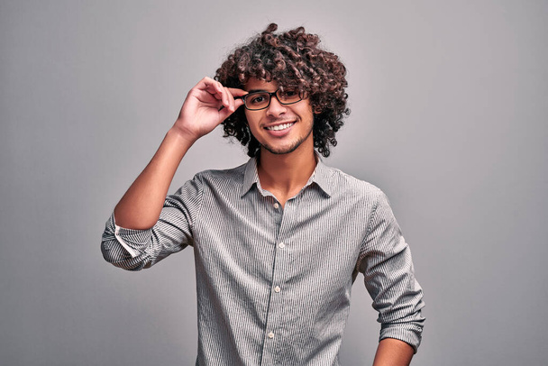 Indian young man in casual clothes adjusting his eyeglasses standing against gray background. Isolated studio image of intelligent handsome man - Photo, Image