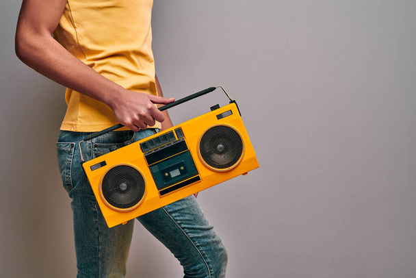 Cropped isolated image of man dressed in casual stylish clothes holding retro stereo tape music player. Boy retro music lover on isolated gray background - 写真・画像