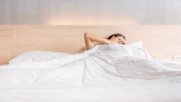 Man waking up and stretching his arm on the bed in white blanket at morning time, laziness concept - 写真・画像