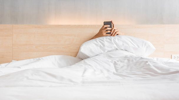 Man waking up and use smartphone or mobile phone on the bed in white blanket at morning time, social lifestyle concept - Foto, immagini