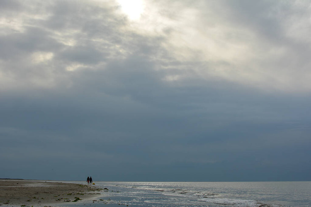 Wieczorny spacer po piaszczystej plaży na wybrzeżu Morza Północnego z zachmurzonym niebem - Zdjęcie, obraz