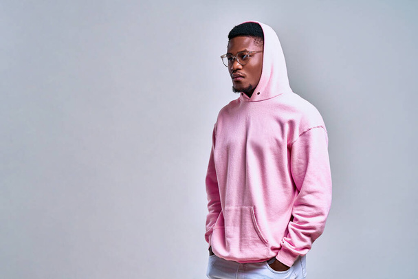 A picture of a stylish african-american man dressed in a pink hoodie with a hood on was taken in the studio on a light red background. Fashion and lifestyle. - Photo, Image