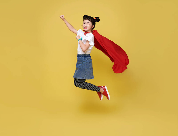 Little child asian girl plays superhero on yellow background studio shot. Girl power hero concept. - Photo, Image