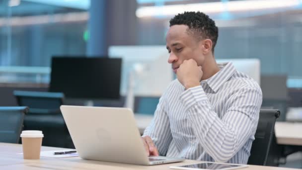 Młody afrykański biznesmen z laptopem myślenie w pracy  - Materiał filmowy, wideo